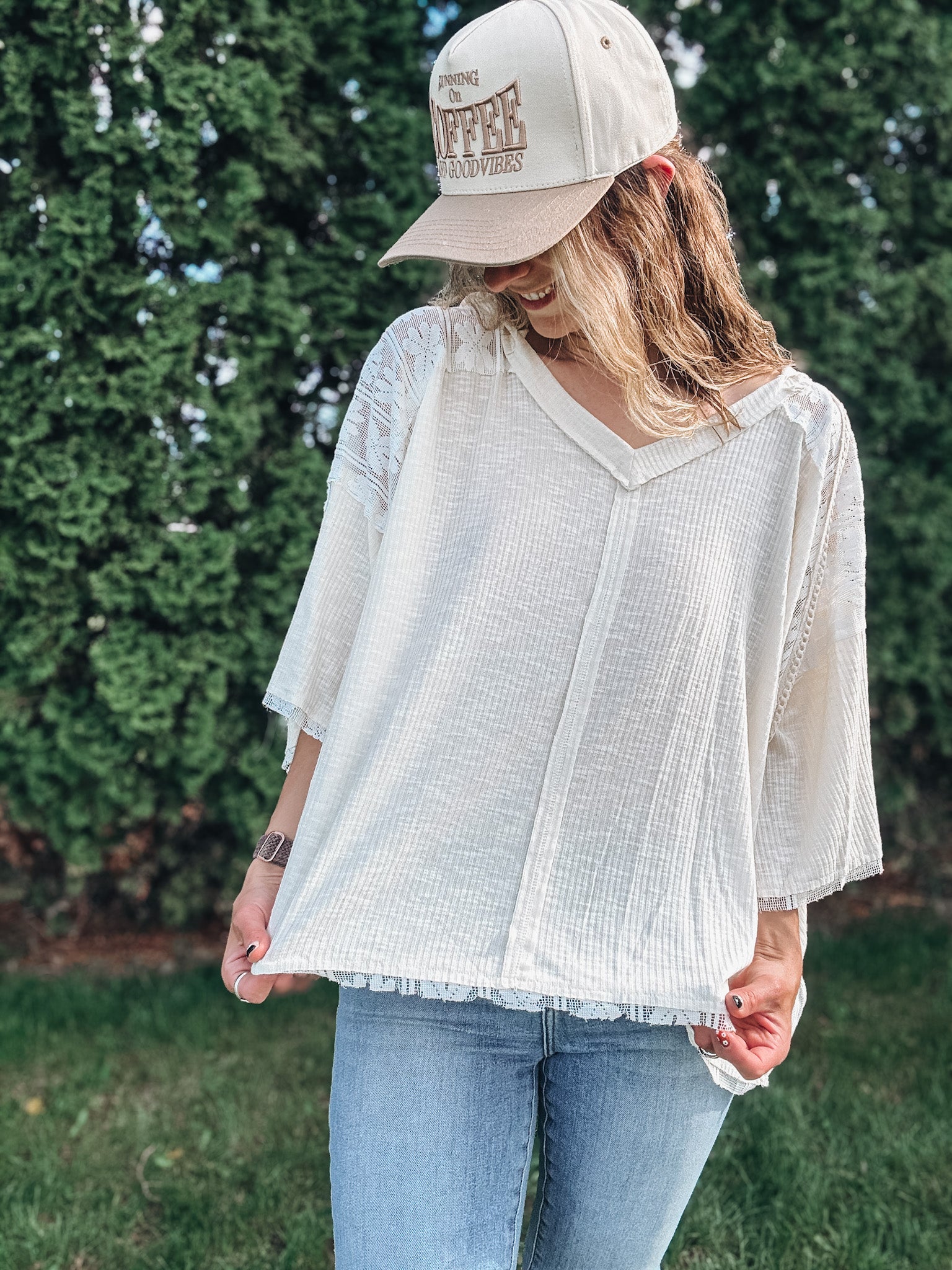 Person wearing a white blouse and beige cap with text, standing outdoors.