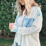 Woman wearing a light blue denim jacket over a white lace top with a beige cap outdoors.