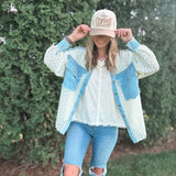 Person wearing a light blue denim jacket with a white shirt and ripped jeans, standing in front of green bushes.