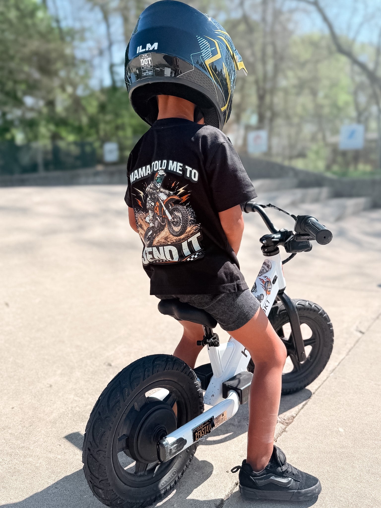 Child wearing a black t-shirt with a graphic and text, sitting on a balance bike.