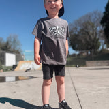 Boy standing at skate park with snapback wearing a gray shirt that says "No Fear Club".