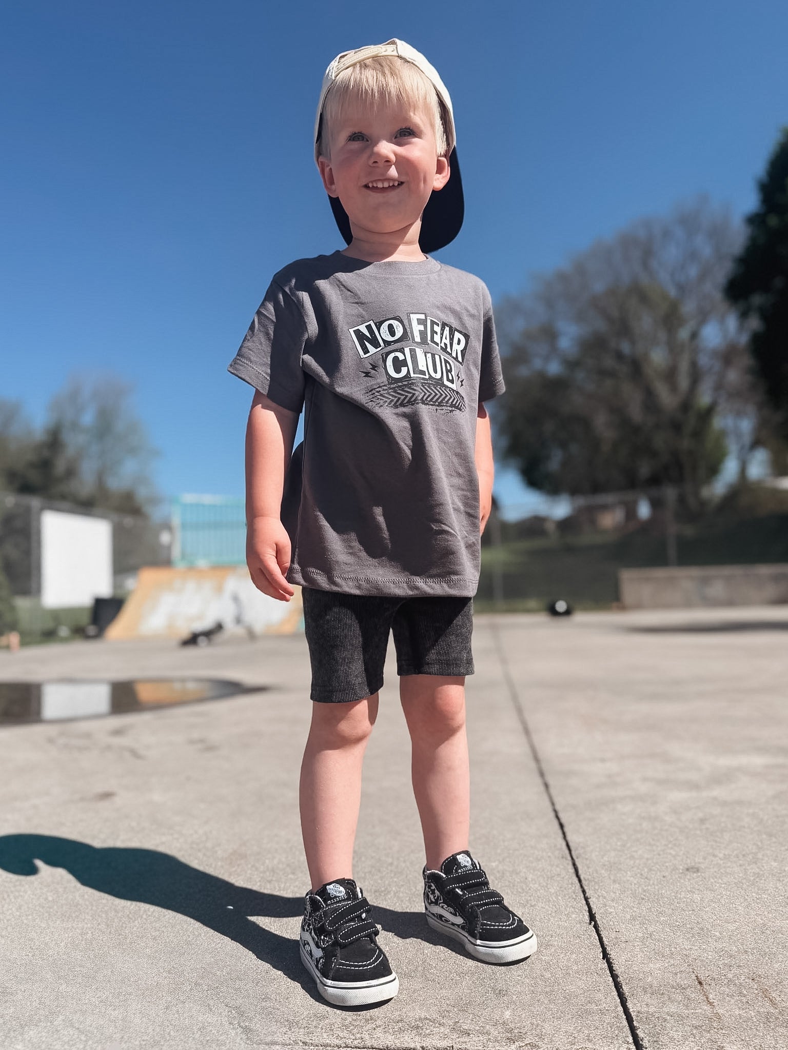 Boy standing at skate park with snapback wearing a gray shirt that says "No Fear Club".