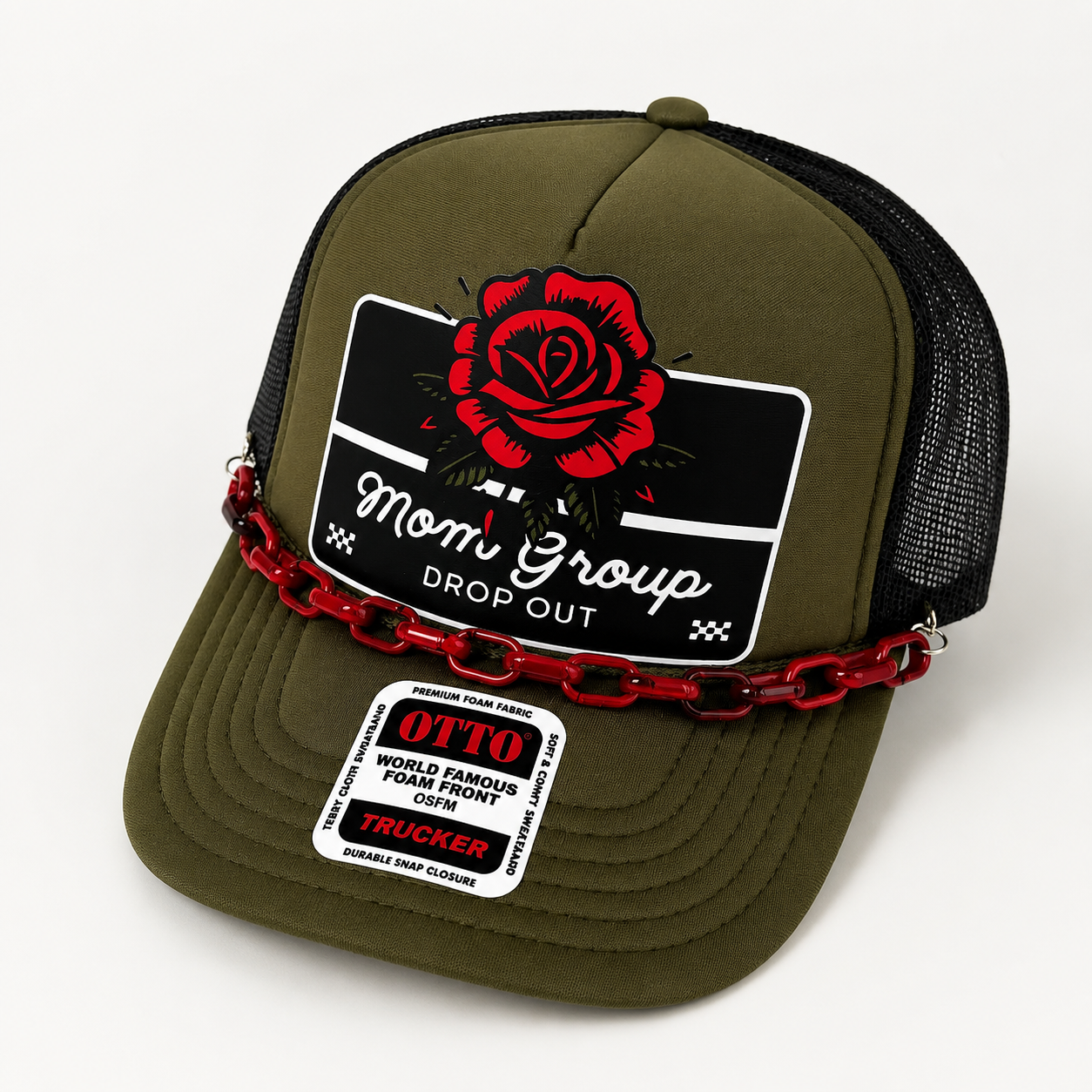 An olive green trucker hat with a black mesh back, featuring a red rose graphic on the front patch that reads 'Mom Group DROP OUT' and a red chain detail across the front. A sewn-on sticker on the brim shows 'OTTO' and 'TRUCKER'.