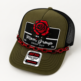 An olive green trucker hat with a black mesh back, featuring a red rose graphic on the front patch that reads 'Mom Group DROP OUT' and a red chain detail across the front. A sewn-on sticker on the brim shows 'OTTO' and 'TRUCKER'.