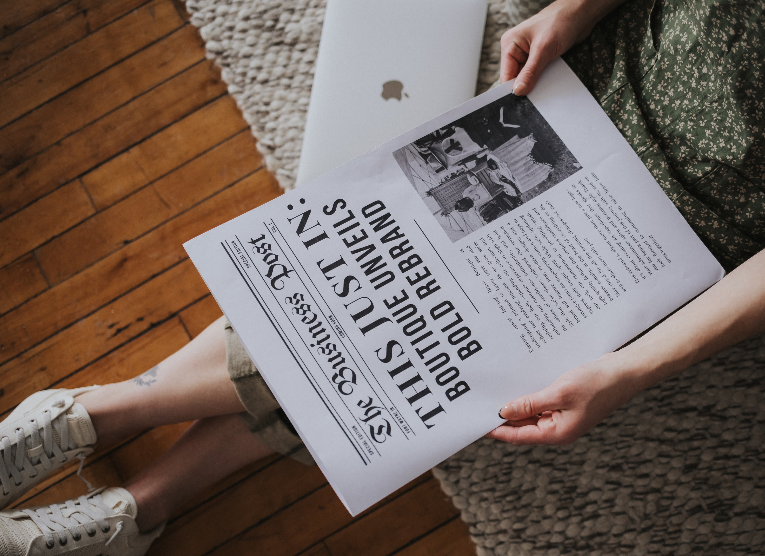 Raising Brave founder sitting on the floor wearing stylish clothing and reading a newspaper headline sharing their rebrand announcement