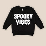 A black long-sleeve sweatshirt with 'SPOOKY VIBES' printed in a white dripping font across the chest, displayed flat against a light beige background.