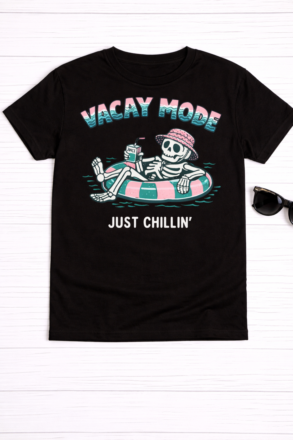 Flat lay photo of a black t-shirt with a skeleton in an inner tube with a juice box. 