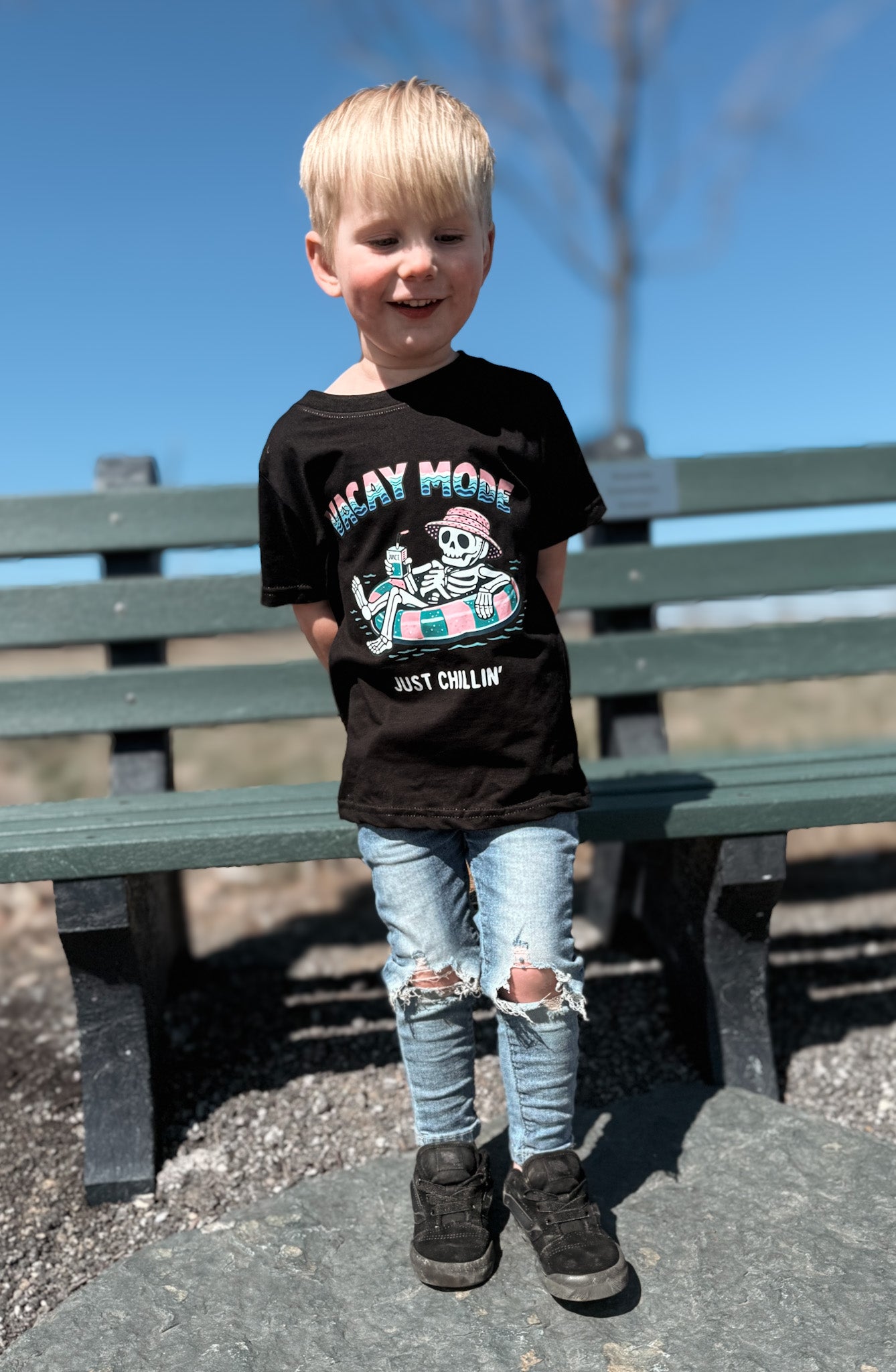 Child wearing a black skeleton Vacay Mode tee outside. 